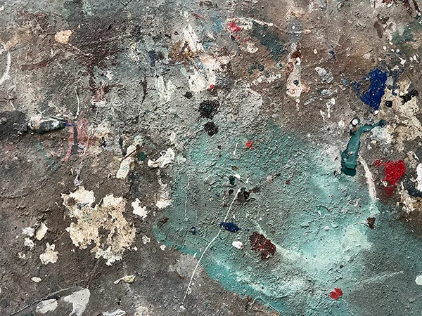 Die Nahaufnahme einer rauen, strukturierten Oberfläche mit Farbklecksen in Teal, Rot, Blau und Weiß erzeugt ein abstraktes, verwittertes Erscheinungsbild - und spiegelt die Kunstfertigkeit unserer Maler- und Glaserwerkstatt.