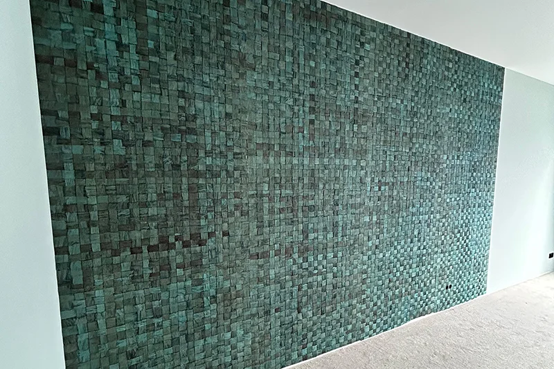 Eine große Akzentwand mit einem strukturierten, mosaikartigen Muster aus grünen und blaugrünen Fliesen, die vom Meisterbetrieb Maler- und Glaserwerkstatt Förster aus der Eifel hergestellt wurde, schafft ein gewebtes Erscheinungsbild inmitten heller Wände und eines neutralen Teppichbodens.